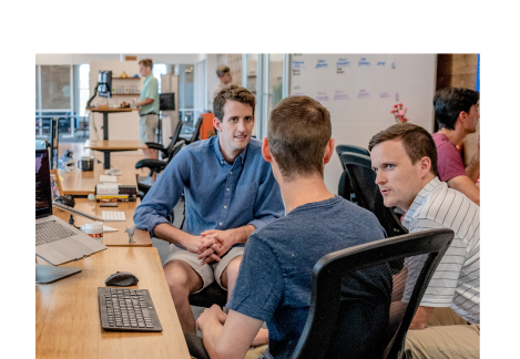 three business men sitting around a desk having a discussion