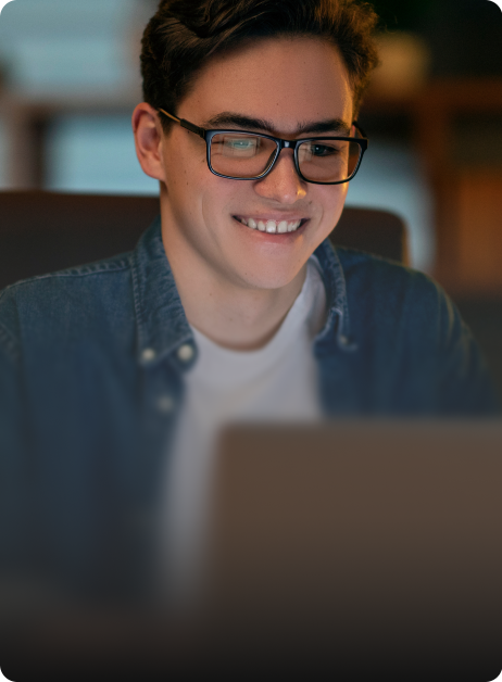 man with glasses smiling while looking on laptop