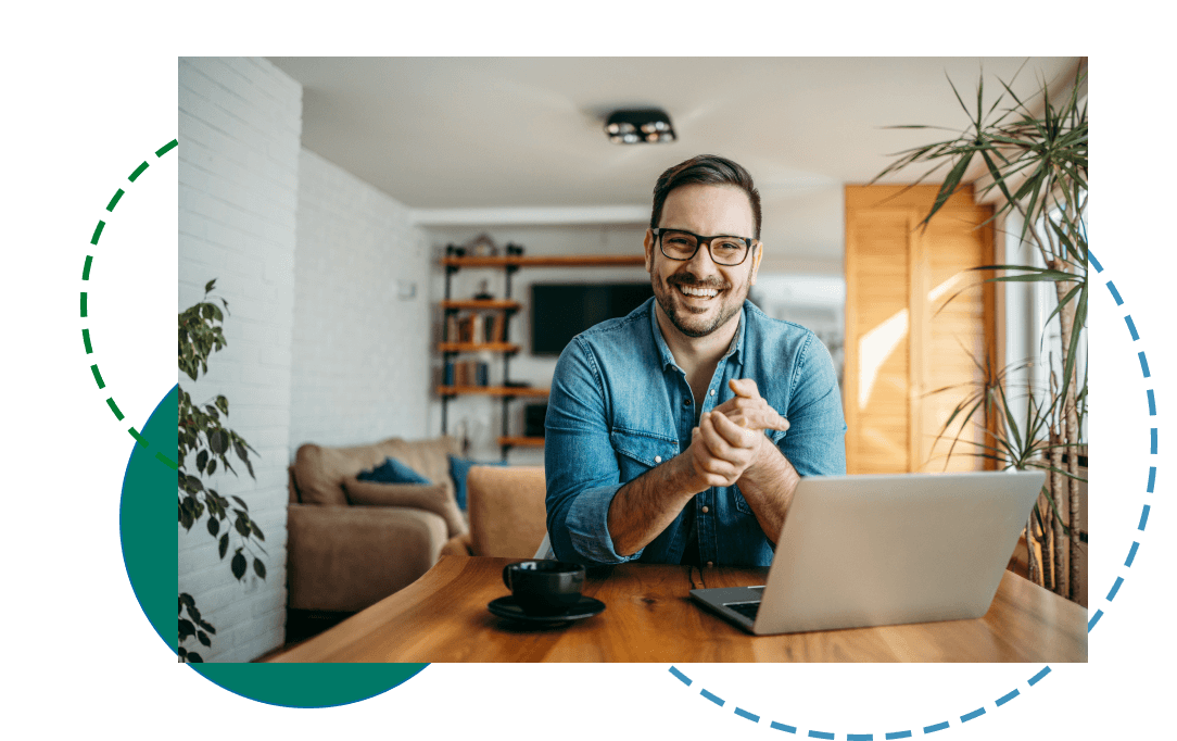 Smiling man sitting at a dining table with a laptop and coffee mug in front of him