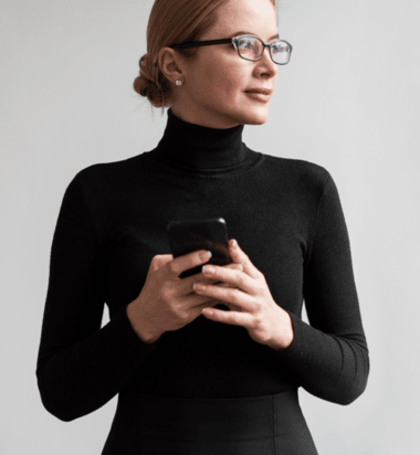 image of woman wearing a black turtleneck and glasses on her phone
